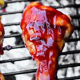 Smoked chicken drumsticks and grilled wings are basted in rich barbecue sauce, sizzling together on a grill with aluminum foil catching every delicious drip.