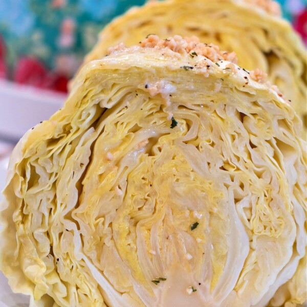 A close-up showcases two cabbage halves on a plate, set against a floral-patterned background, evoking the cozy aroma of a whole head of cabbage slowly simmering in a slow cooker.