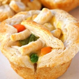 A mini chicken pot pie muffin with a flaky crust, topped with carrots, peas, and a lattice of dough strips.