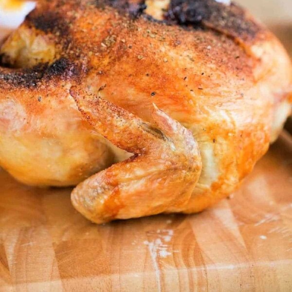 Roasted whole chicken on a wooden cutting board, seasoned with visible spices. The golden-brown, crispy skin hints at the perfection achieved even with a pressure-cooked frozen whole chicken, its wing prominently facing upward.