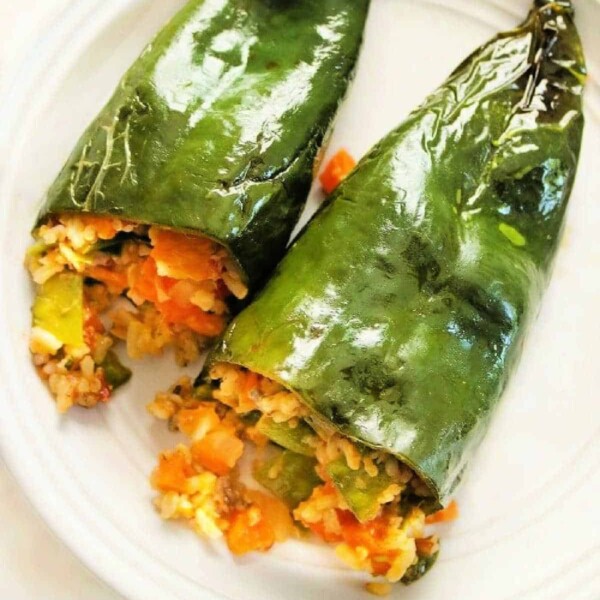 Two grilled stuffed peppers, bursting with rice and vegetables, rest invitingly on a white plate.