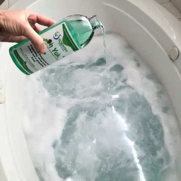 A hand pours liquid soap into a jetted tub filled with water and bubbles. The bottle, with its green label, complements the gleaming white oval-shaped bathtub as it effortlessly tackles the task of cleaning.