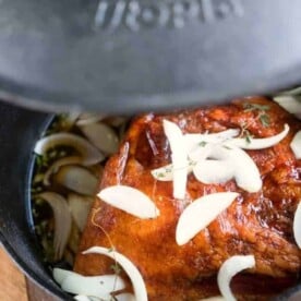 Ham with onions and herbs simmers perfectly in a black pot, partly covered with a lid—an ideal addition to your collection of Dutch oven recipes.