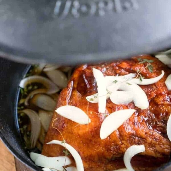 Ham with onions and herbs simmers perfectly in a black pot, partly covered with a lid—an ideal addition to your collection of Dutch oven recipes.