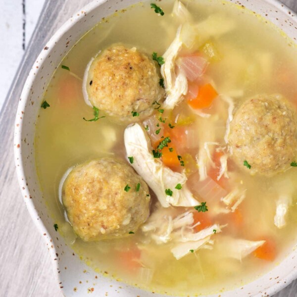 A bowl of rich Chicken Matzo Ball Soup sits invitingly on a wooden surface, brimming with tender chicken and vibrant vegetables.