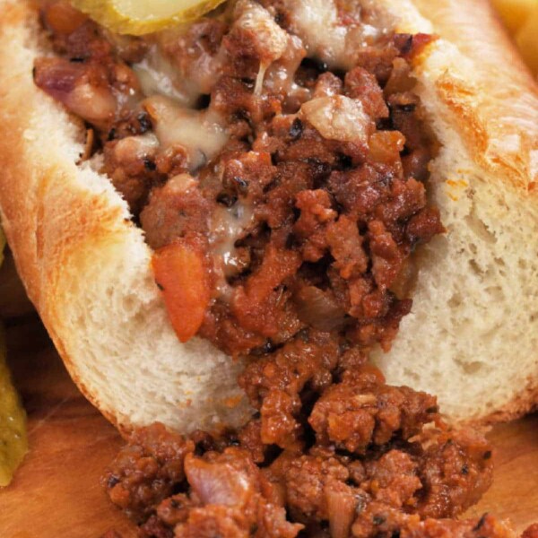 A hoagie with seasoned minced meat, reminiscent of homemade Sloppy Joes recipes, topped with pickle slices, sits enticingly on a wooden board.