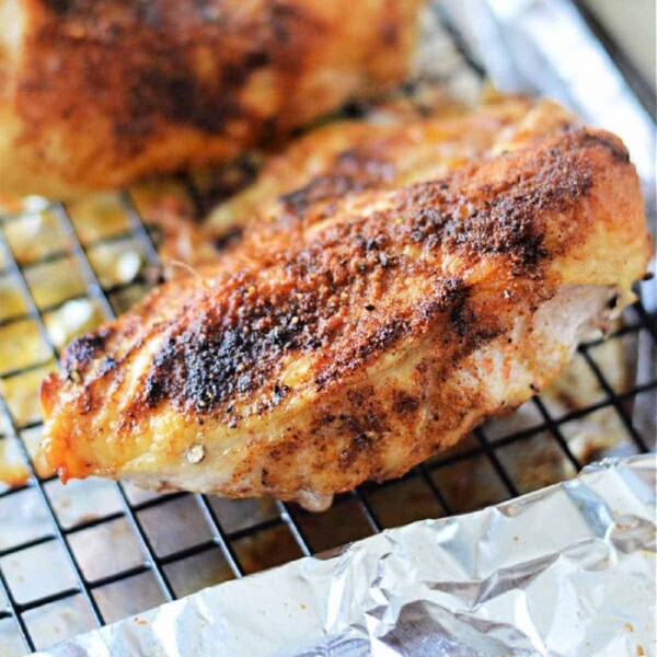 A piece of cooked chicken breast with a crispy, seasoned skin rests on a wire rack over aluminum foil. Perfectly cooked at 400 degrees for the right amount of time, the seasoning is evenly distributed, giving the chicken a golden-brown appearance.