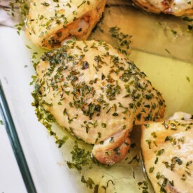 Boiled chicken thighs with herbs and garlic in a glass dish, offering a flavorful alternative for those wondering how long to boil chicken thighs.