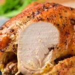 Roasted whole chicken with golden skin, reminiscent of learning how to cook a whole chicken to perfection, cut to reveal tender white meat and elegantly garnished with parsley in the background.