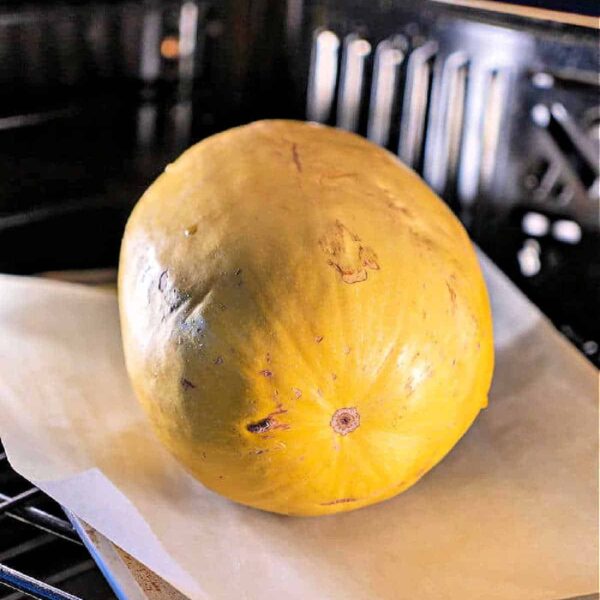 Whole spaghetti squash sits on parchment paper, roasting to perfection in the oven.