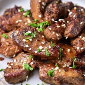 Grilled beef pieces garnished with sesame seeds and chopped parsley share the spotlight on a round ceramic plate, complemented by succulent slices of pork liver.