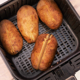 Four whole potatoes, with slits on top, are ready to reheat as they sit neatly in the air fryer basket.