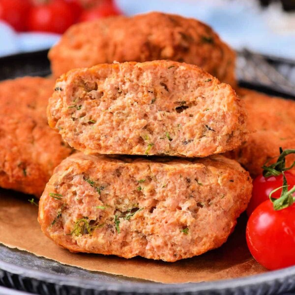 Close-up of two stacked, sliced Old Fashioned Salmon Patties on a tray with a fresh tomato garnish in the background.