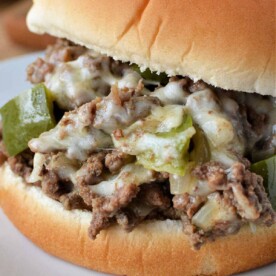 Close-up of a Sloppy Joe sandwich with ground beef, melted cheese, and green peppers on a white plate, evoking the savory essence of a Philly Cheesesteak.