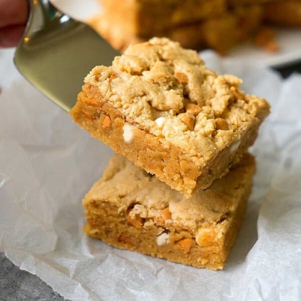 A spatula lifts a square cake mix peanut butter brownie stuffed with peanut butter chips, placed on parchment paper.