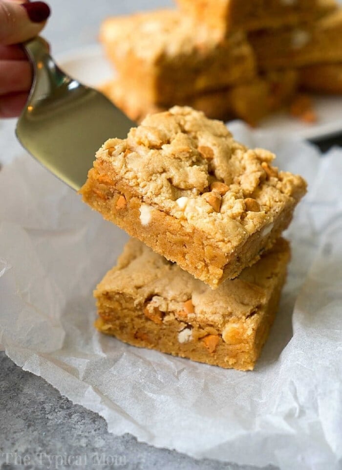 A spatula lifts a square cake mix peanut butter brownie stuffed with peanut butter chips, placed on parchment paper.