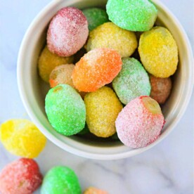 A bowl of colorful, sugar-coated grapes sits on a marble surface, resembling a delightful tutorial on how to make candied grapes with Jello.