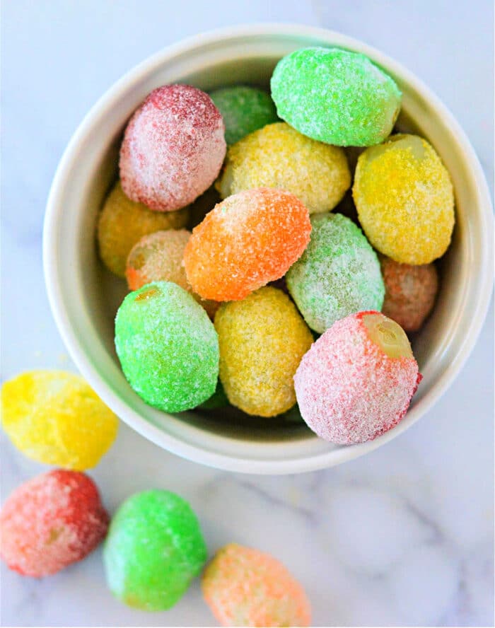 A bowl of colorful, sugar-coated grapes sits on a marble surface, resembling a delightful tutorial on how to make candied grapes with Jello.