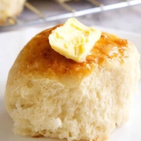 A buttered dinner roll on a plate, made even more delightful by starting with frozen rolls.