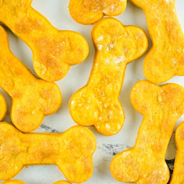 Air fryer dog treats, shaped like bones and delightfully orange, are neatly arranged on a white surface.