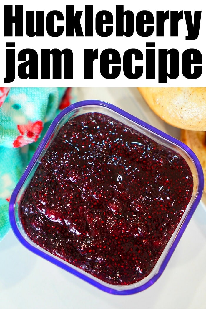 A container of huckleberry jam with a blue rim rests gracefully on a surface beside a charmingly patterned cloth.