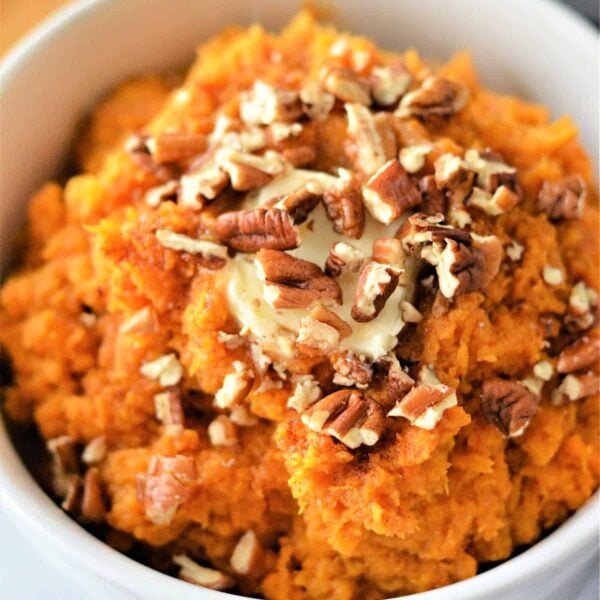 A bowl of creamy mashed sweet potatoes, reminiscent of air fryer mashed potatoes, is topped with a pat of melting butter and crunchy chopped pecans.