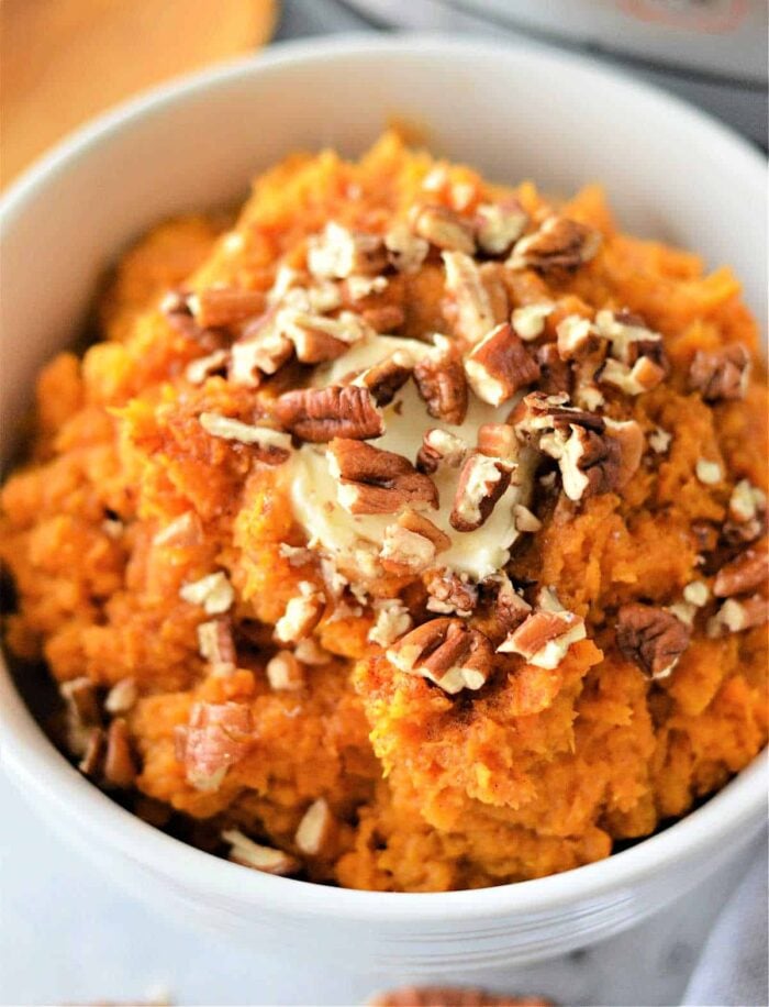 A bowl of creamy mashed sweet potatoes, reminiscent of air fryer mashed potatoes, is topped with a pat of melting butter and crunchy chopped pecans.