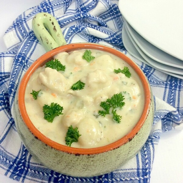 A bowl of creamy instant pot gnocchi soup with chunks of vegetables and parsley garnish, placed on a blue and white checkered cloth beside stacked white plates.