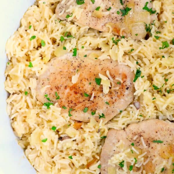 pork chops on a bed of seasoned rice, garnished with chopped parsley—a perfect meal to enjoy alongside ninja foodi pork chops.
