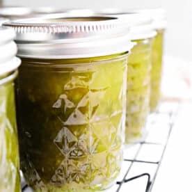 Close-up of jars filled with green Pepper Jelly and relish, sealed with metal lids, cooling on a wire rack.