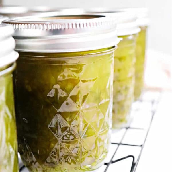 Close-up of jars filled with green Pepper Jelly and relish, sealed with metal lids, cooling on a wire rack.