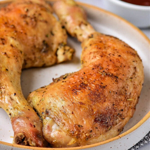 Two roasted chicken leg quarters on a round plate, seasoned and cooked to golden brown perfection. An Instant Pot sits in the background, hinting at the flavorful journey. A bowl with sauce is visible for that extra touch of indulgence.