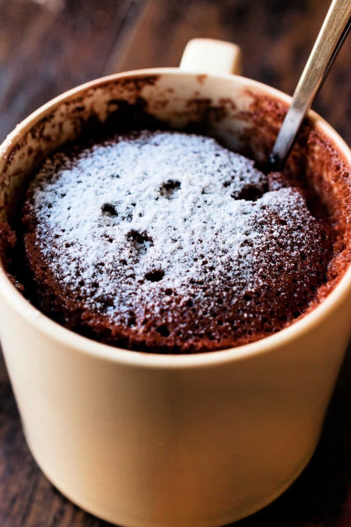 A Chocolate Mayonnaise Cake with Cake Mix transformed into a mug cake, topped with powdered sugar and served with a spoon inside the mug.