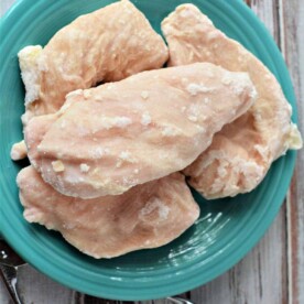 A turquoise plate holds frozen chicken breasts, elegantly displayed on a rustic wooden table.