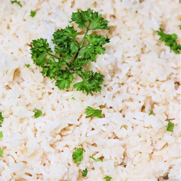 A close-up of cooked rice, garnished with sprigs of fresh parsley, invites the question: how long does rice take to cook to perfection?