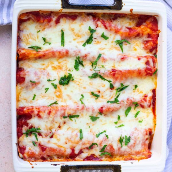 Baked enchiladas topped with melted cheese and fresh herbs in a square dish on a striped cloth, perfectly done after cooking to perfection.