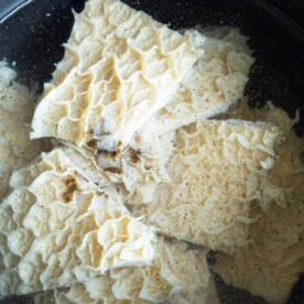 A pot filled with pieces of raw tripe soaking in water, providing a glimpse into how to cook tripe. The textured, ruffled surface suggests it's in the preparation stage. The clear water contrasts with the black pot, setting the scene for a culinary journey.