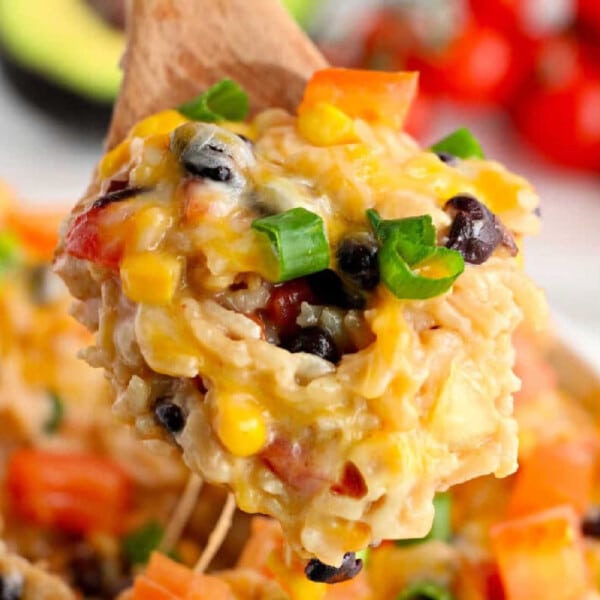 A wooden spoon holds cheesy rice with black beans, corn, and diced tomatoes, garnished with green onions—an instant pot Mexican chicken and rice delight.