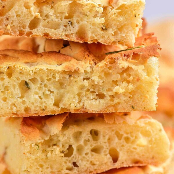 Stack of golden, fluffy sourdough focaccia slices garnished with fresh herbs on top.