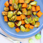A delicious plate featuring perfectly roasted Brussels sprouts and sweet potatoes sits invitingly, with a fork poised beside it, ready to dive into this wholesome delight.