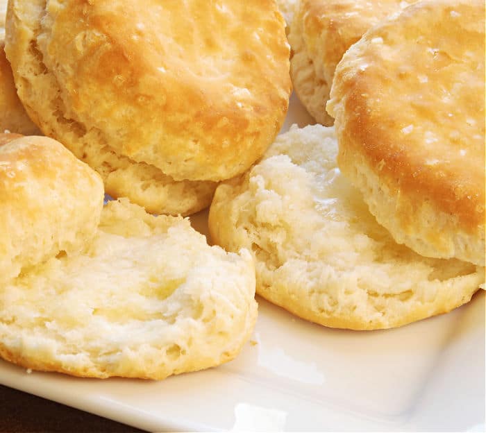 Golden, flaky air fryer biscuits on a white plate, with one biscuit split open to reveal its soft, fluffy interior.