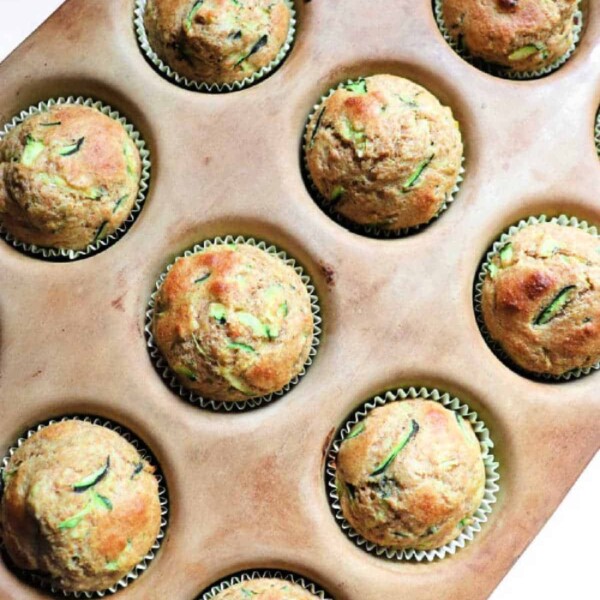 A muffin tray holds 12 freshly baked zucchini applesauce muffins, each nestled perfectly in paper liners.