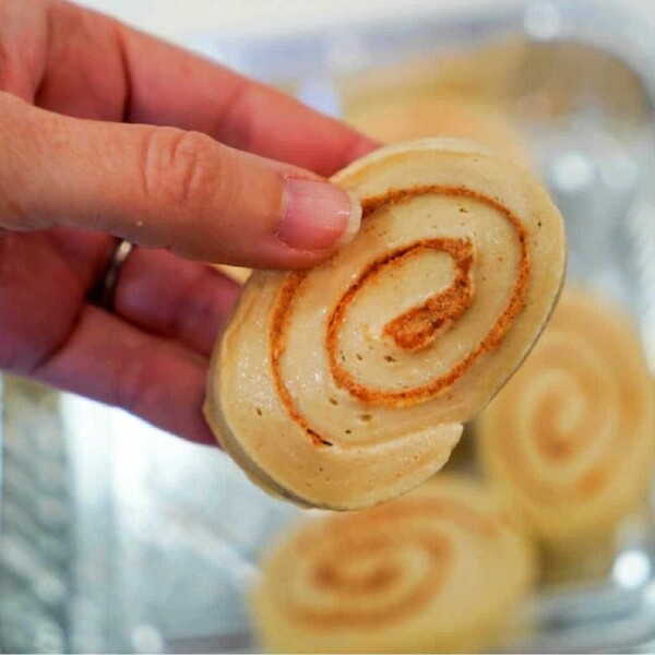 Close-up of a hand holding a cinnamon roll swirl with more frozen cinnamon rolls in the background.