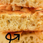 A mouthwatering close-up of sliced sourdough focaccia, delicately sprinkled with fresh herbs and appetizingly stacked. The text beautifully highlights: Sourdough Focaccia.