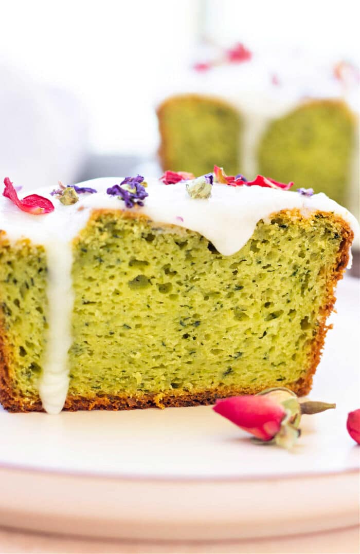 Slice of delightful avocado cake with white frosting, topped with dried flowers, presented elegantly on a plate.