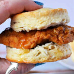 Close-up of a hand holding a biscuit sandwich with fried chicken and honey butter. Text: Copycat Whataburger Honey Butter Chicken Biscuit—bringing the beloved flavors of this Southern favorite to your kitchen.