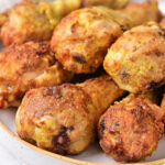 Golden brown curry fried chicken drumsticks stacked on a white plate.
