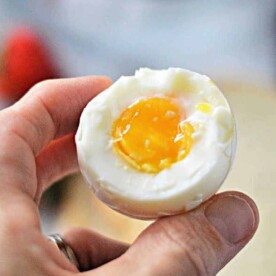 A hand holding a half-peeled soft-boiled egg reveals a perfectly runny yolk, the result of knowing just how long to cook soft boiled eggs on the stove.