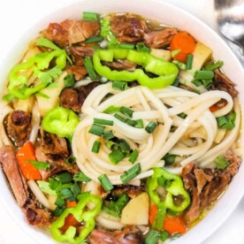 A bowl of oxtail pho brimming with vegetables, beef, and chives, garnished with green peppers.