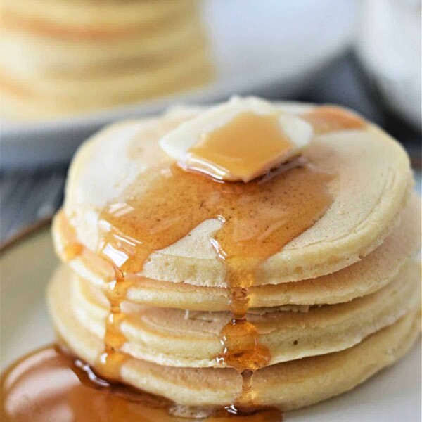 A stack of fluffy pancakes made without baking powder, topped with melting butter and syrup on a white plate.